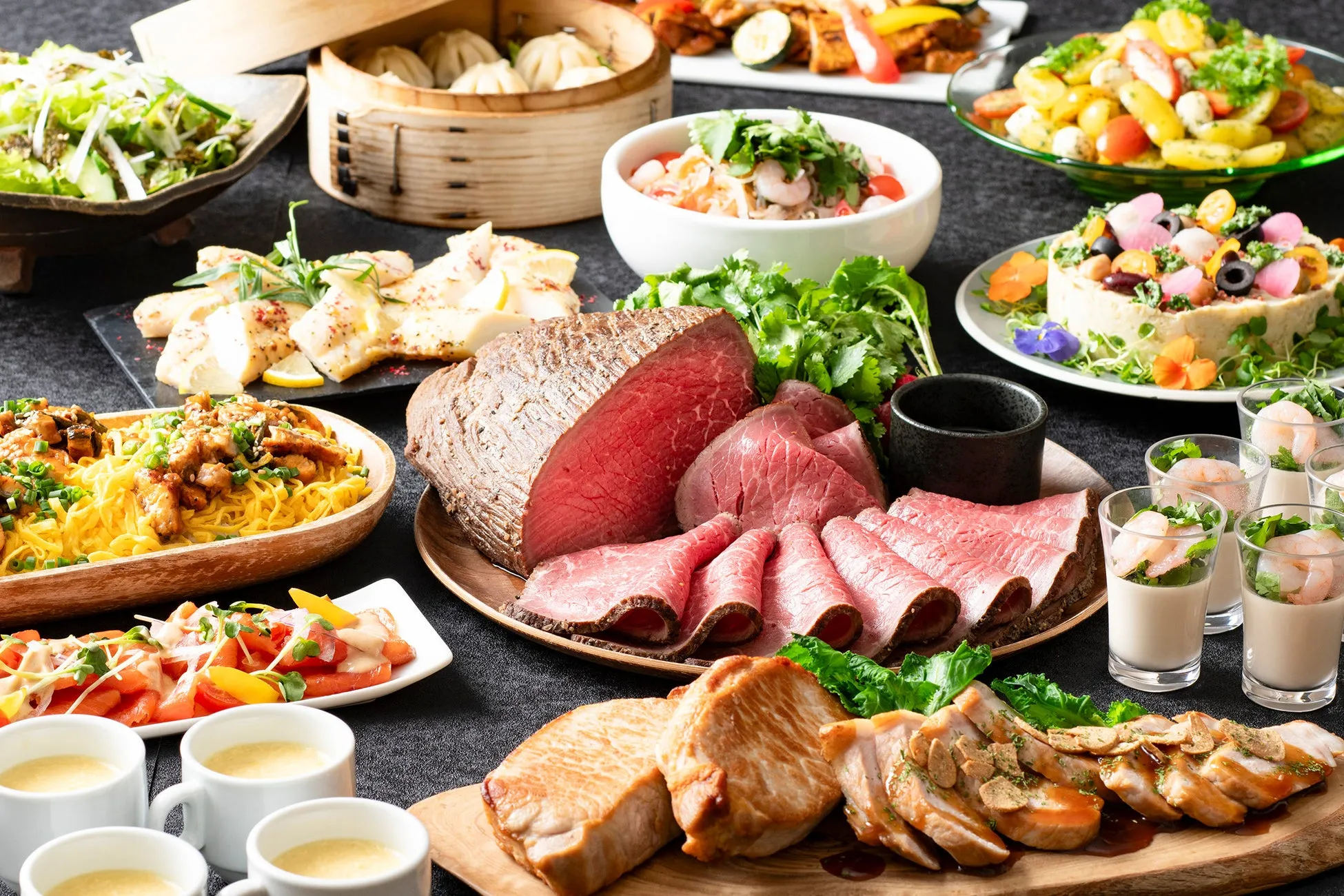 様々な料理がテーブルに並べられた、美味しそうな食事の風景です。ローストビーフ、点心、サラダ、スープ、麺類、魚料理、エビ料理など、彩り豊かで食欲をそそります。パーティーやビュッフェを想起させる華やかな雰囲気です。