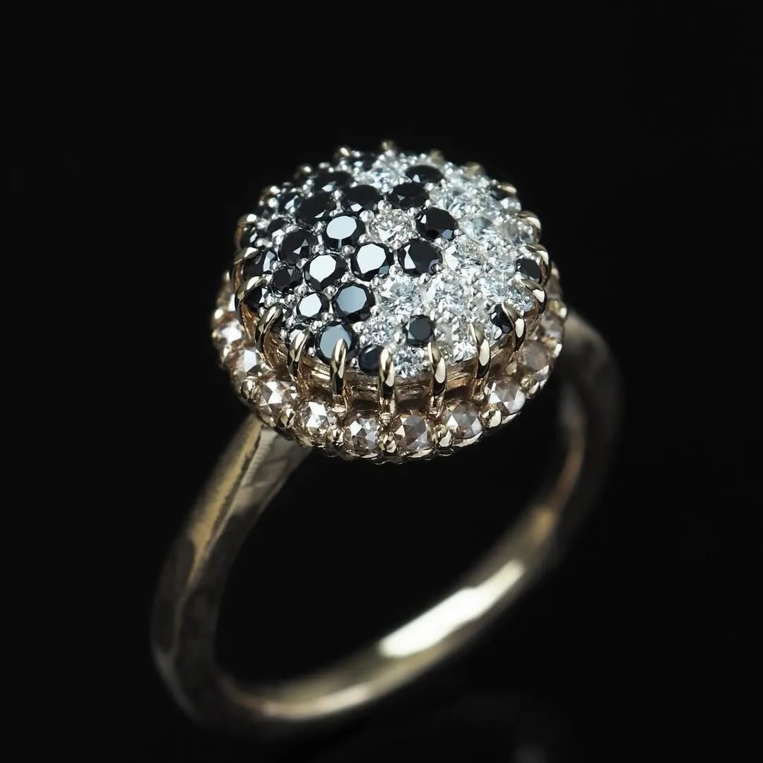 黒と白の宝石が散りばめられたリング。リングは金色の金属で作られており、黒い背景に配置されています。