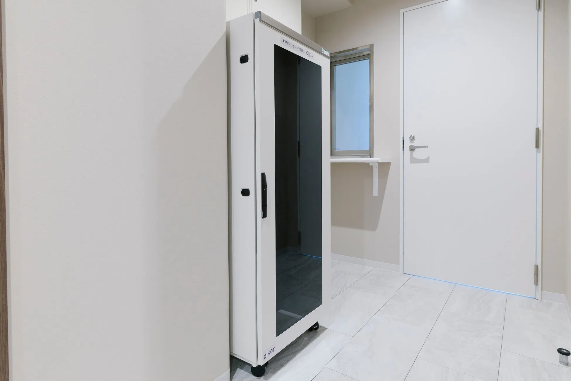 白いキャビネットと白いドアがある部屋の画像。キャビネットには非常用バックアップ電源と書かれた文字が見える。