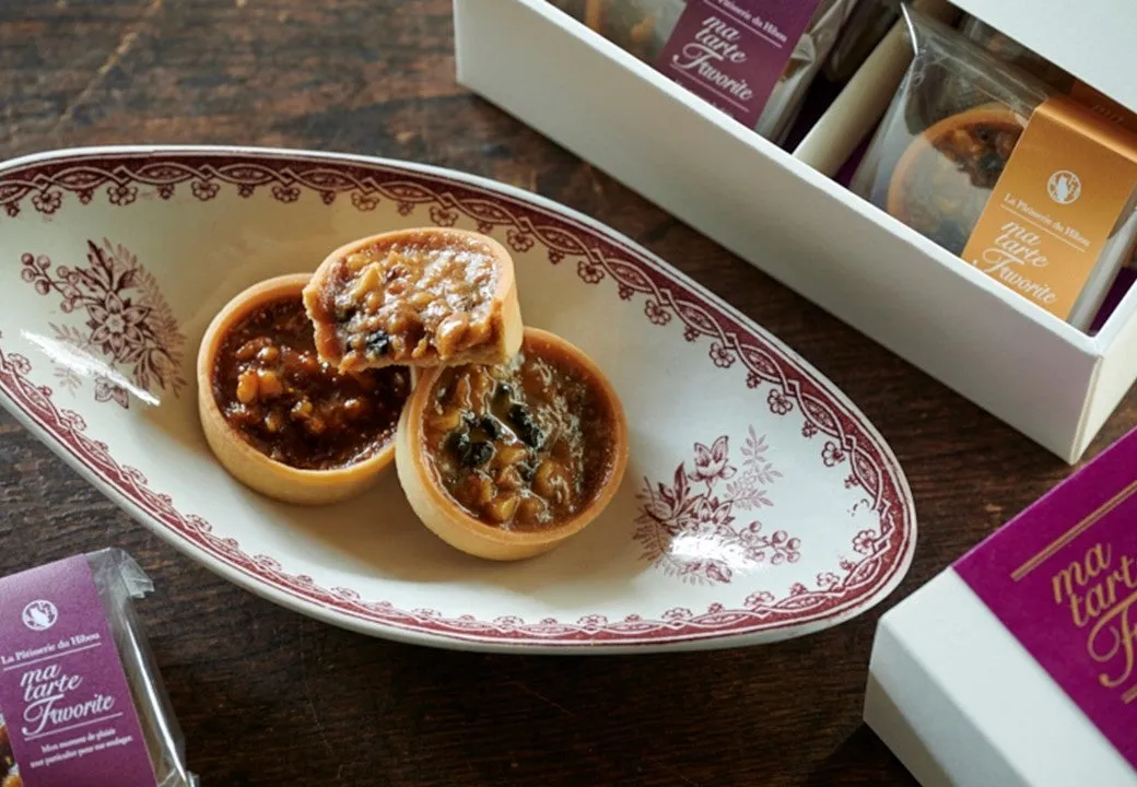 お皿に載ったタルトの写真。タルトは、ナッツやジャムのようなものでトッピングされています。箱に入ったタルトも写っています。