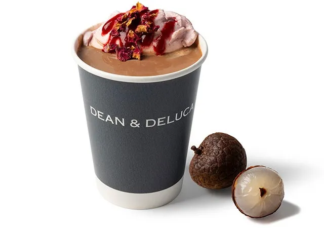 DEAN & DELUCAのカップに入ったチョコレートドリンク。トッピングにはクリームとドライフラワーのようなものが乗せられ、横にはライチが添えられている。