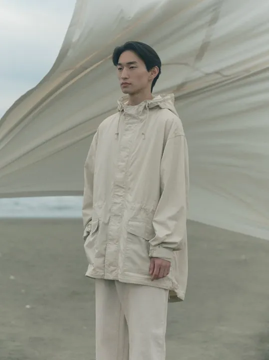 砂浜に立つベージュのフード付きジャケットとパンツの男性モデル