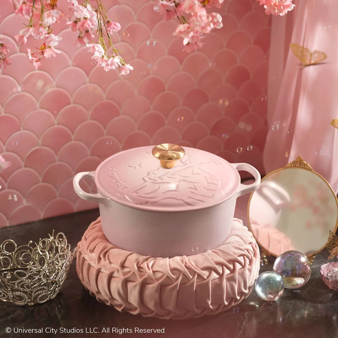 ピンク色の鍋が、ピンク色のクッションの上に置かれています。背景にはピンク色の壁、桜の枝、鏡、ティアラなどがあり、全体的に可愛らしい雰囲気です。