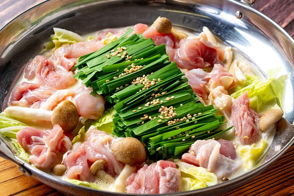 鍋料理の写真。鶏肉、野菜、きのこなどが煮込まれており、白濁したスープが特徴的。