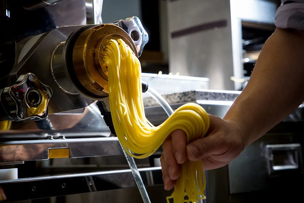 パスタメーカーから作られたばかりのパスタを手で掴んでいる様子。