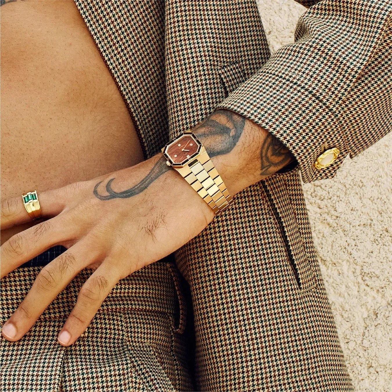 男性が金色の時計と指輪を身につけ、チェック柄のジャケットを着ている様子。