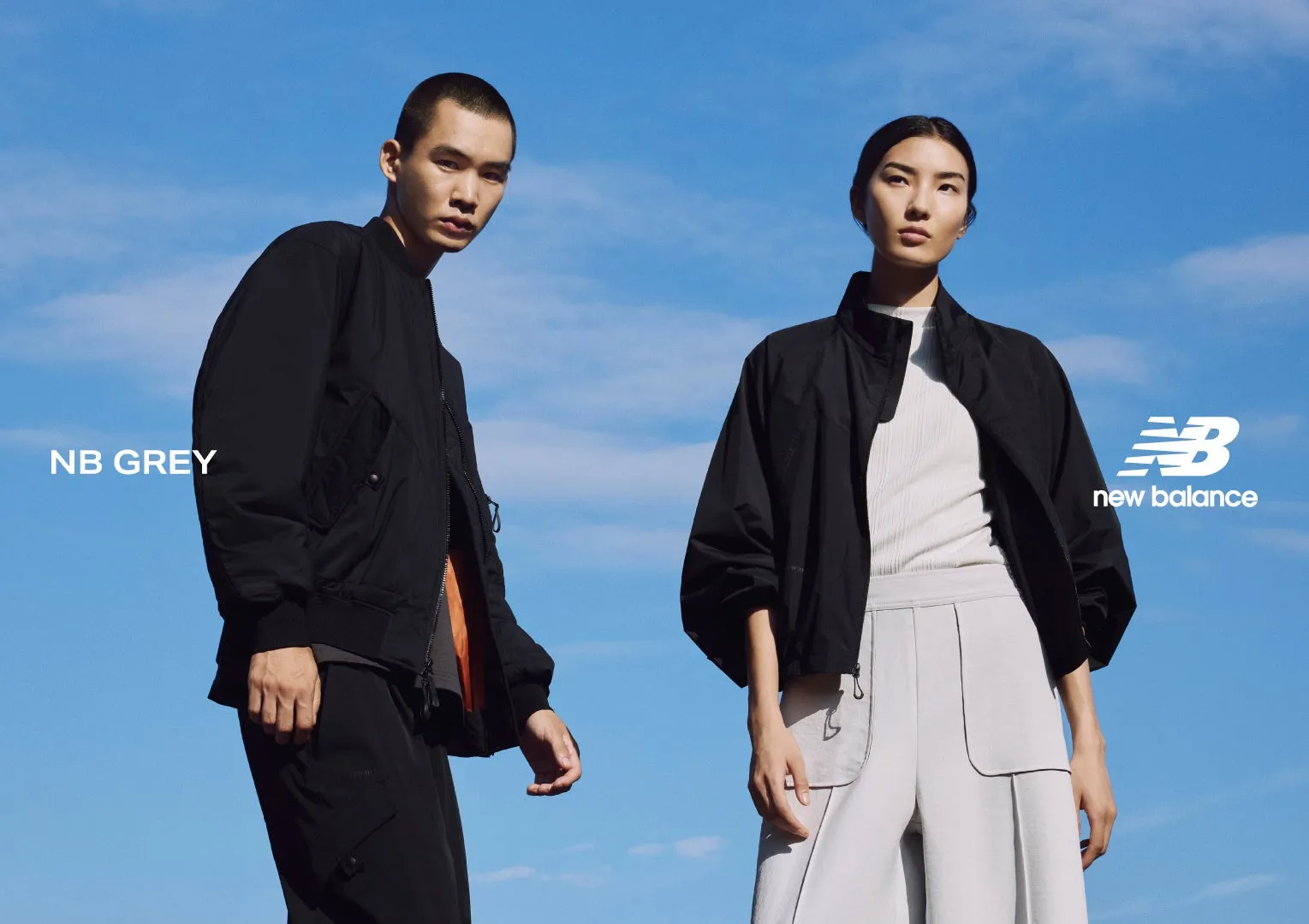 2人のモデルが黒いジャケットを着て、青空を背景にポーズをとっている画像です。