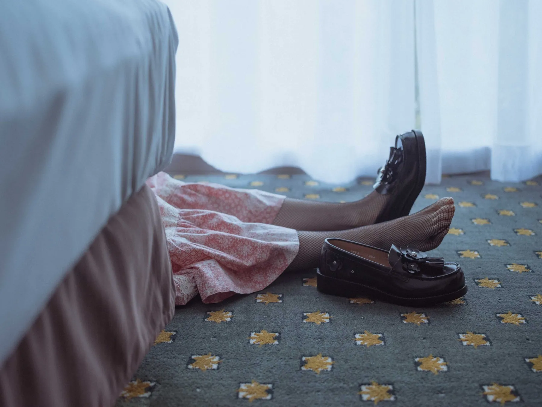 ベッドの横で網タイツと革靴を履く女性