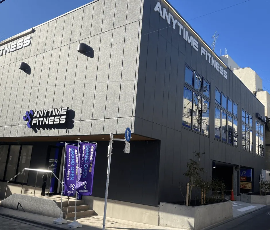 Anytime Fitnessの建物の外観写真。青い看板には「GRAND OPEN」の文字が見える。