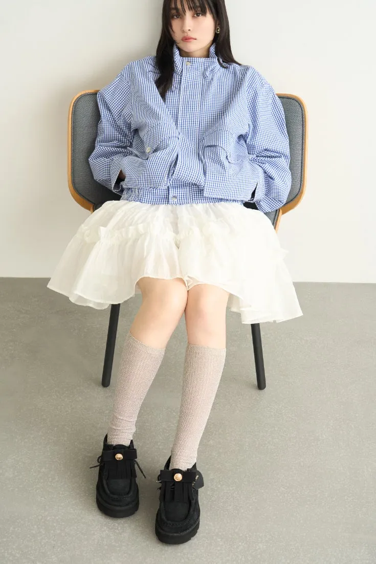 女性が、青いギンガムチェックのジャケット、白いミニスカート、ベージュのハイソックス、黒い靴を着用して立っている写真