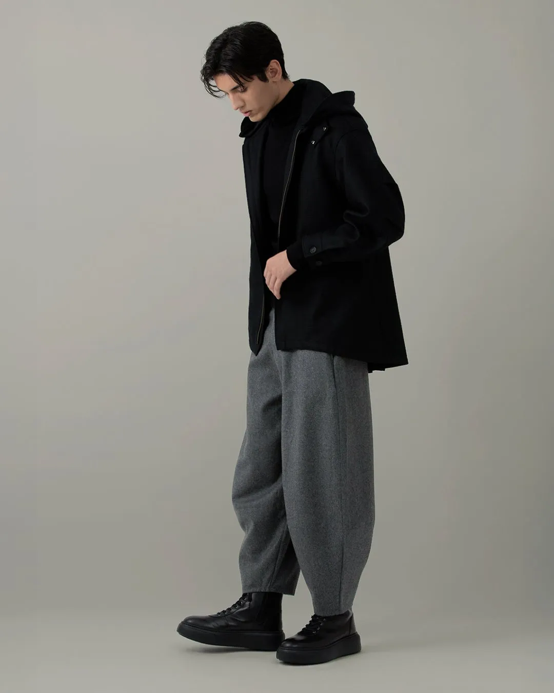 黒いフード付きジャケットとグレーのバルーンパンツを着た男性