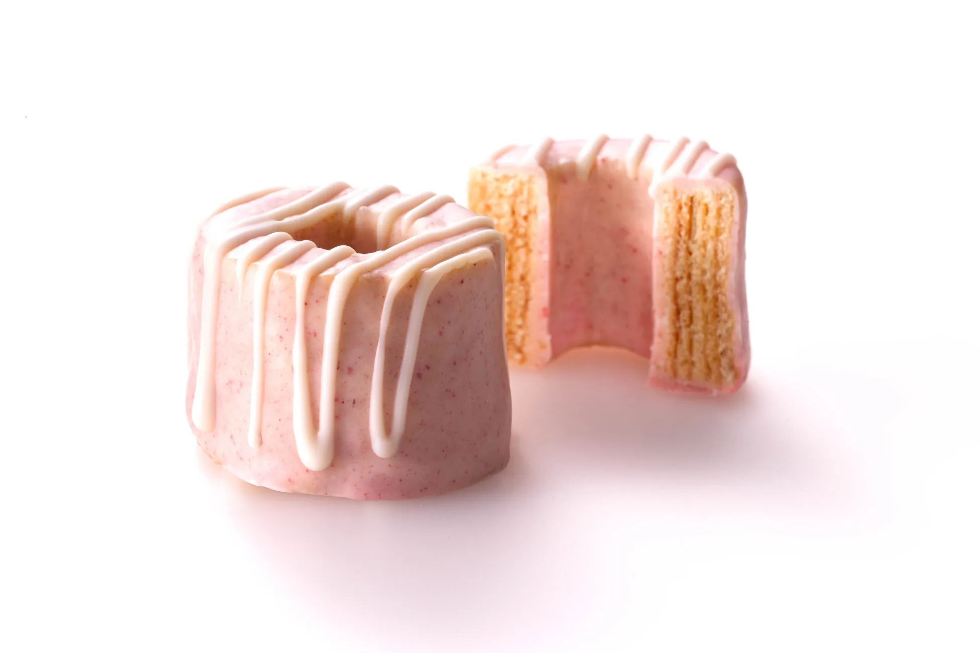 ピンク色のケーキが2つ並んだ写真。ケーキは円柱形で、上に白いアイシングがかけられています。一つは半分にカットされており、内部の層が見えます。