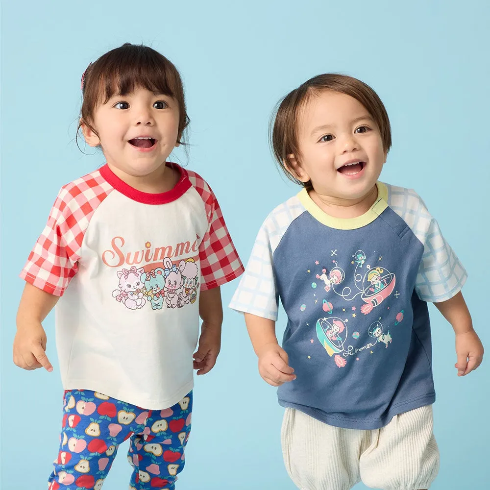 2人の子供が笑顔で写っている写真。子供たちは、それぞれ異なるデザインのTシャツを着ています。左の子供は、赤いチェック柄の袖と「Swimmi」の文字が入った白いTシャツを着ており、青いリンゴ柄のパンツを履いています。右の子供は、青色のTシャツを着ており、宇宙をテーマにしたデザインが施されています。背景は青色です。