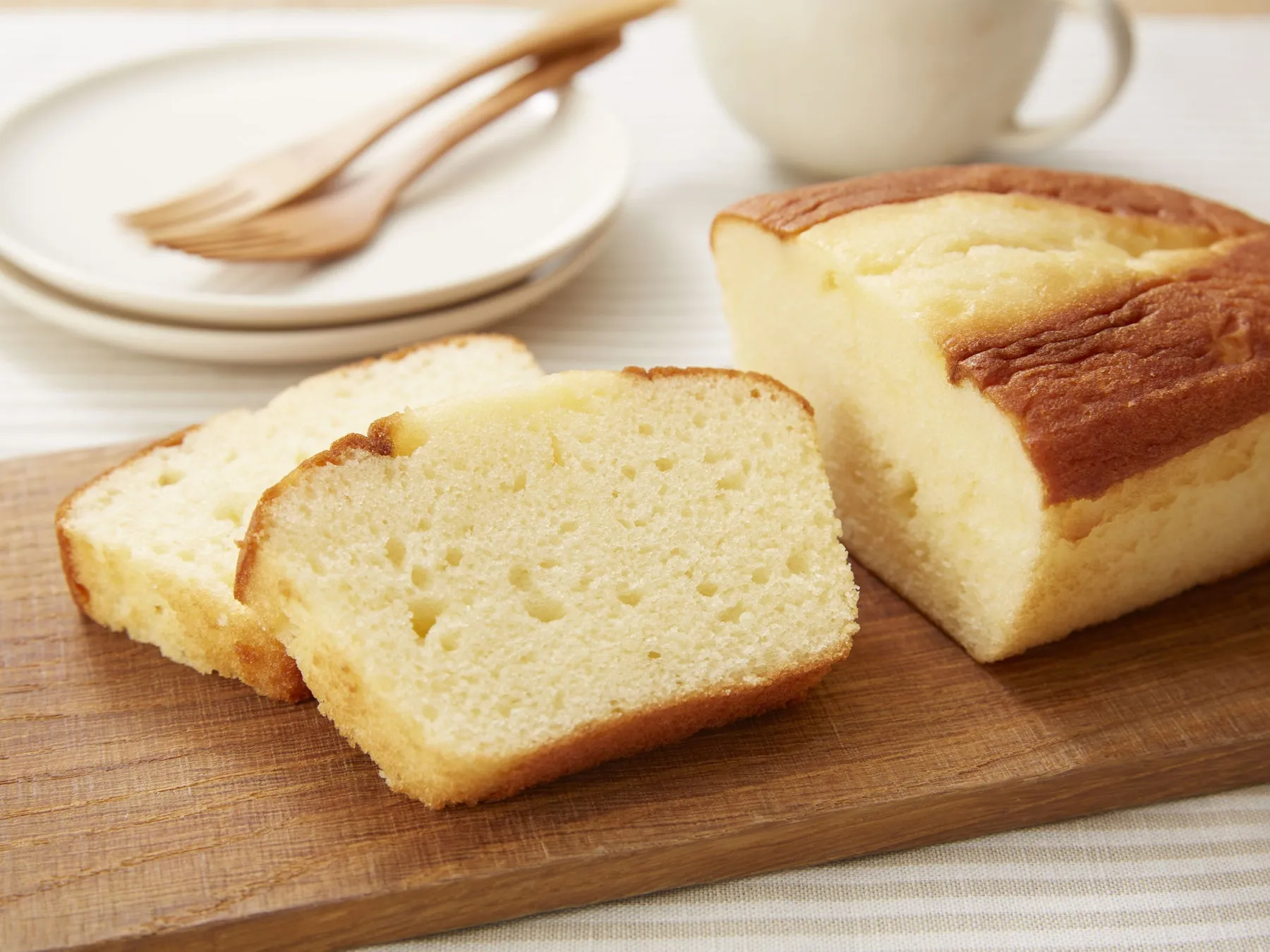 木製のまな板の上に、パウンドケーキが置かれています。パウンドケーキはカットされており、断面が見えています。さらに、皿とフォーク、カップが写っています。