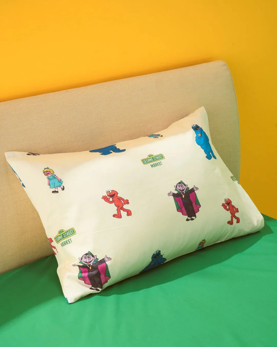 セサミストリートのキャラクターがプリントされた枕が置かれたベッドの写真です。エルモ、クッキーモンスター、伯爵、そしてその他のキャラクターが描かれています。