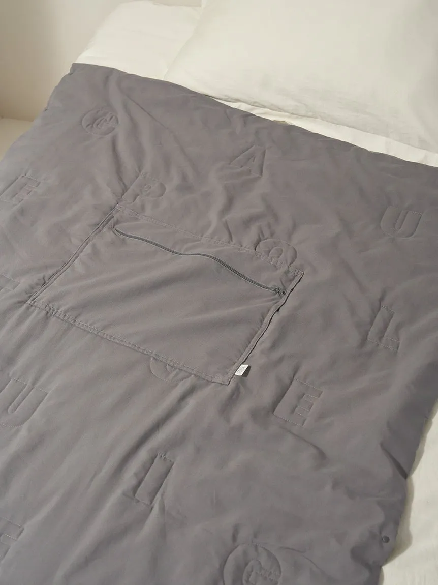 グレーの布団がベッドに掛けられている様子。布団には文字のような模様とジッパー付きのポケットが付いている。