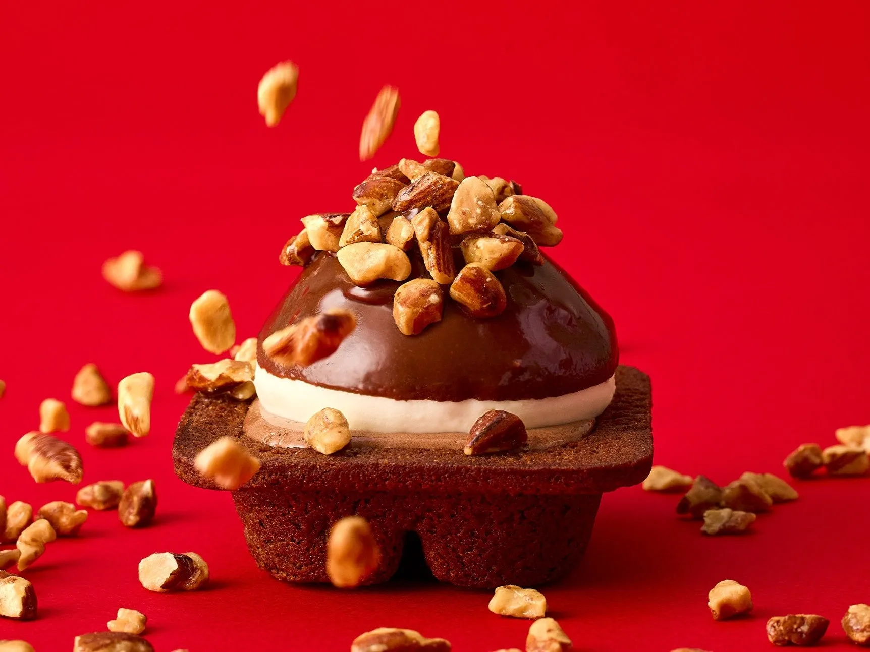 赤い背景に、チョコレートでコーティングされたケーキにナッツがトッピングされています。