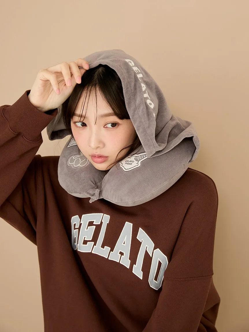 女性が茶色のスウェットシャツを着て、フード付きのネックピローを被っている写真。彼女はカメラの方向を見ています。