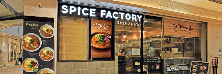 カレーを提供するお店の外観です。「SPICE FACTORY」という店名が大きく書かれており、メニューの看板には料理の写真が掲載されています。店内には「Be Yourself!」という文字も見えます。