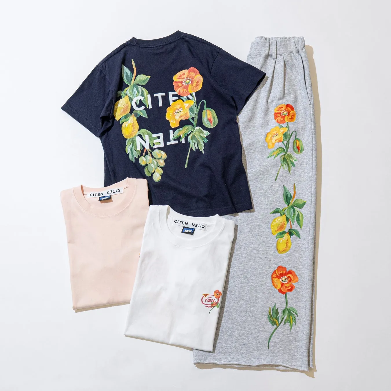 花とフルーツのイラストがプリントされたTシャツとスウェットパンツのセット。Tシャツは紺、ピンク、白の3色展開で、スウェットパンツはグレー。ロゴもプリントされている。