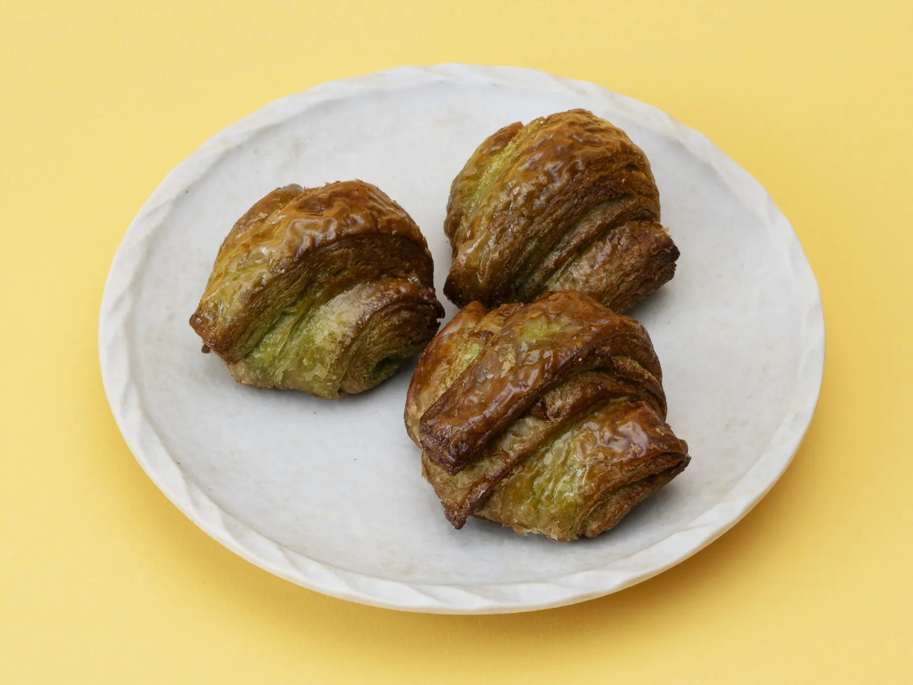 白い皿に3つのパンが乗っている写真です。パンは茶色と緑色をしており、表面は光沢があります。背景は黄色です。