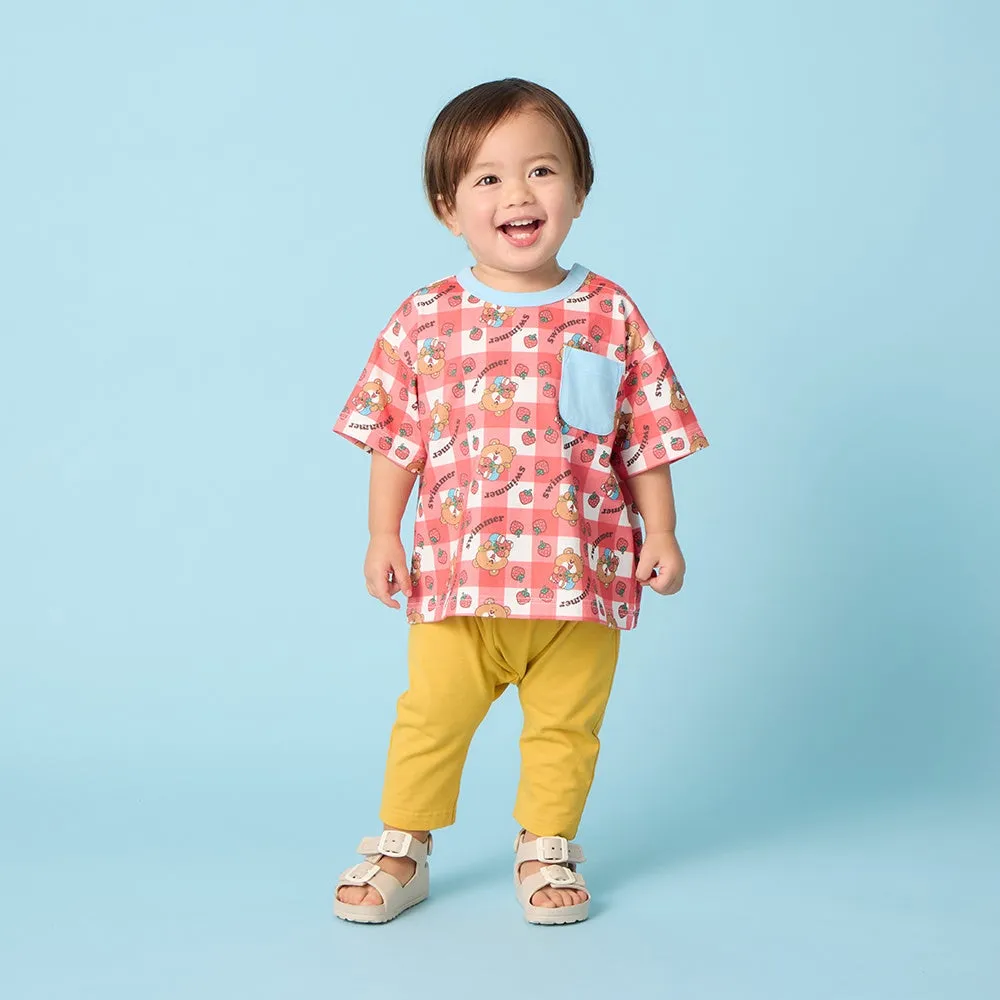 青い背景に、笑顔の子供が半袖Tシャツと黄色いパンツを着て立っている様子。