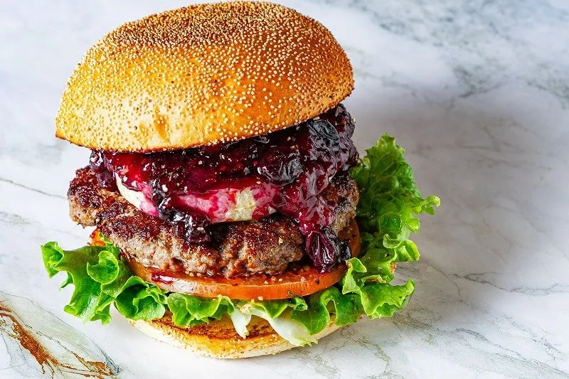 ハンバーガーのクローズアップ写真。バンズ、パティ、レタス、トマト、チーズ、ジャムが使われている。