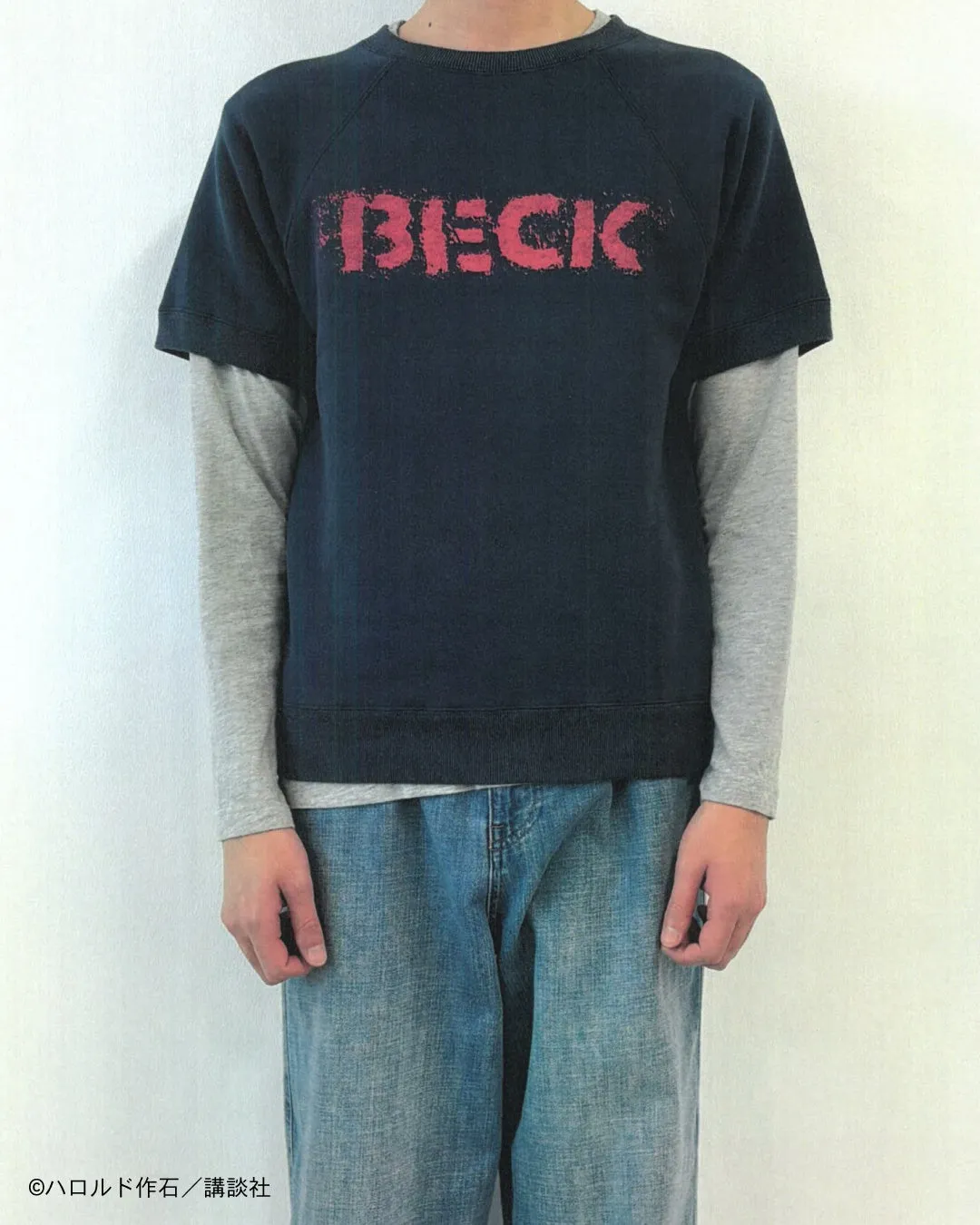 「BECK」のロゴが入ったTシャツを着た人物の画像。重ね着をしており、カジュアルな印象を与える。背景はシンプルな白い壁。