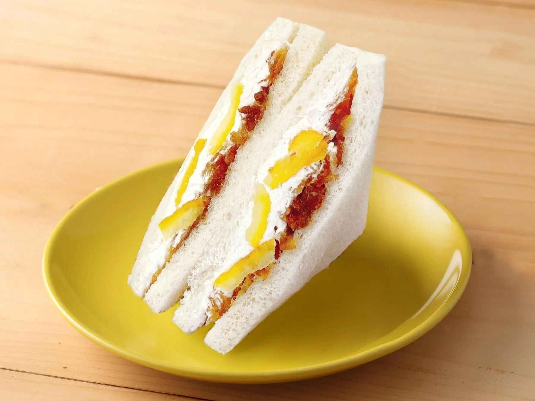 黄色い皿に乗ったサンドイッチのクローズアップです。サンドイッチは、白いパン、白いクリーム、レモン、赤いジャムで構成されています。