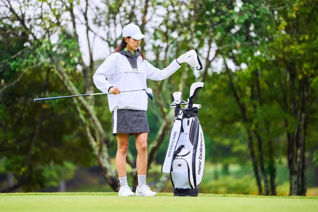 ゴルフウェアを着た女性がゴルフ場でゴルフクラブとゴルフバッグを持っています。