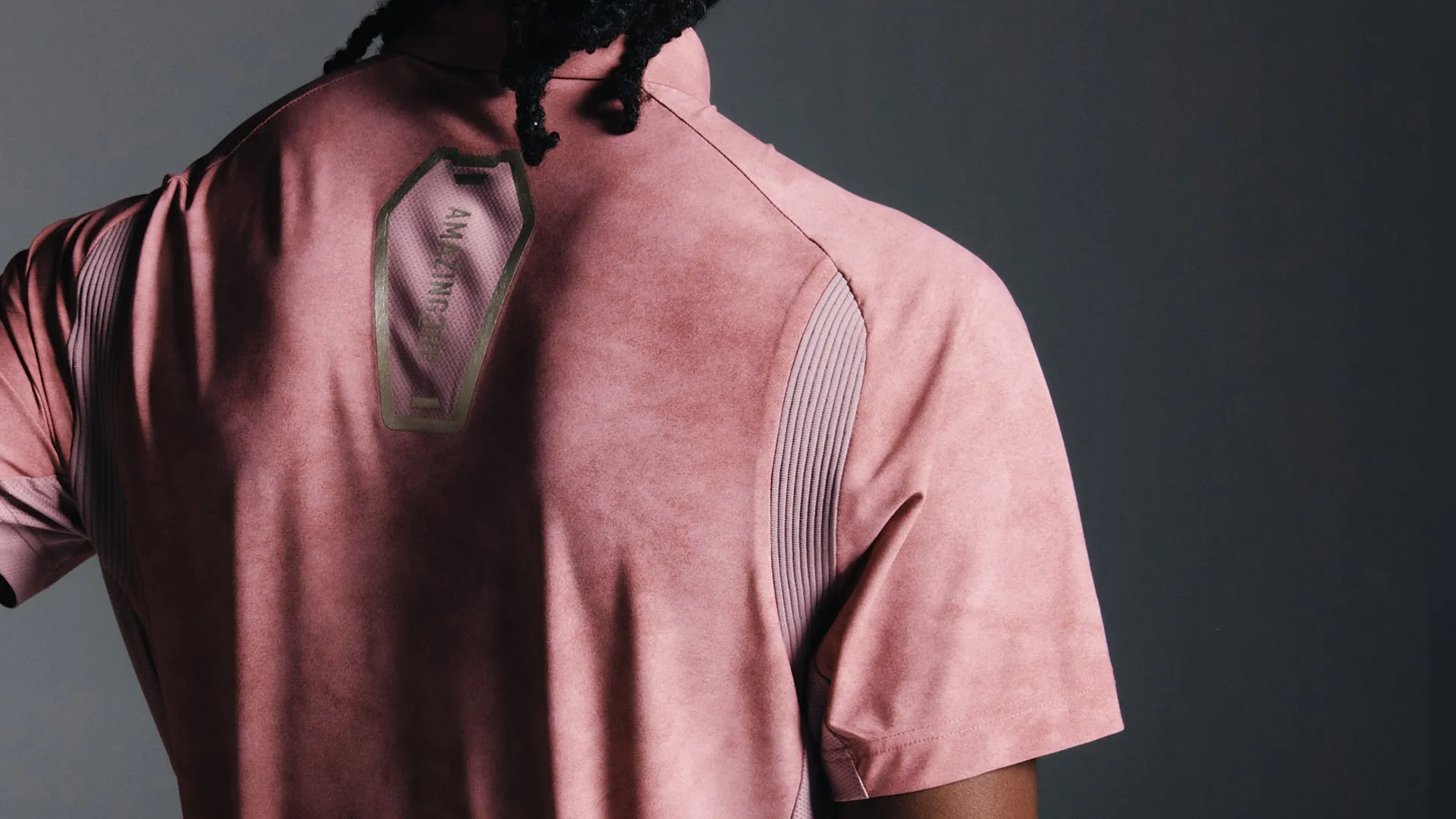 ピンクのTシャツを着た男性の背中、AMAZING COREのロゴ