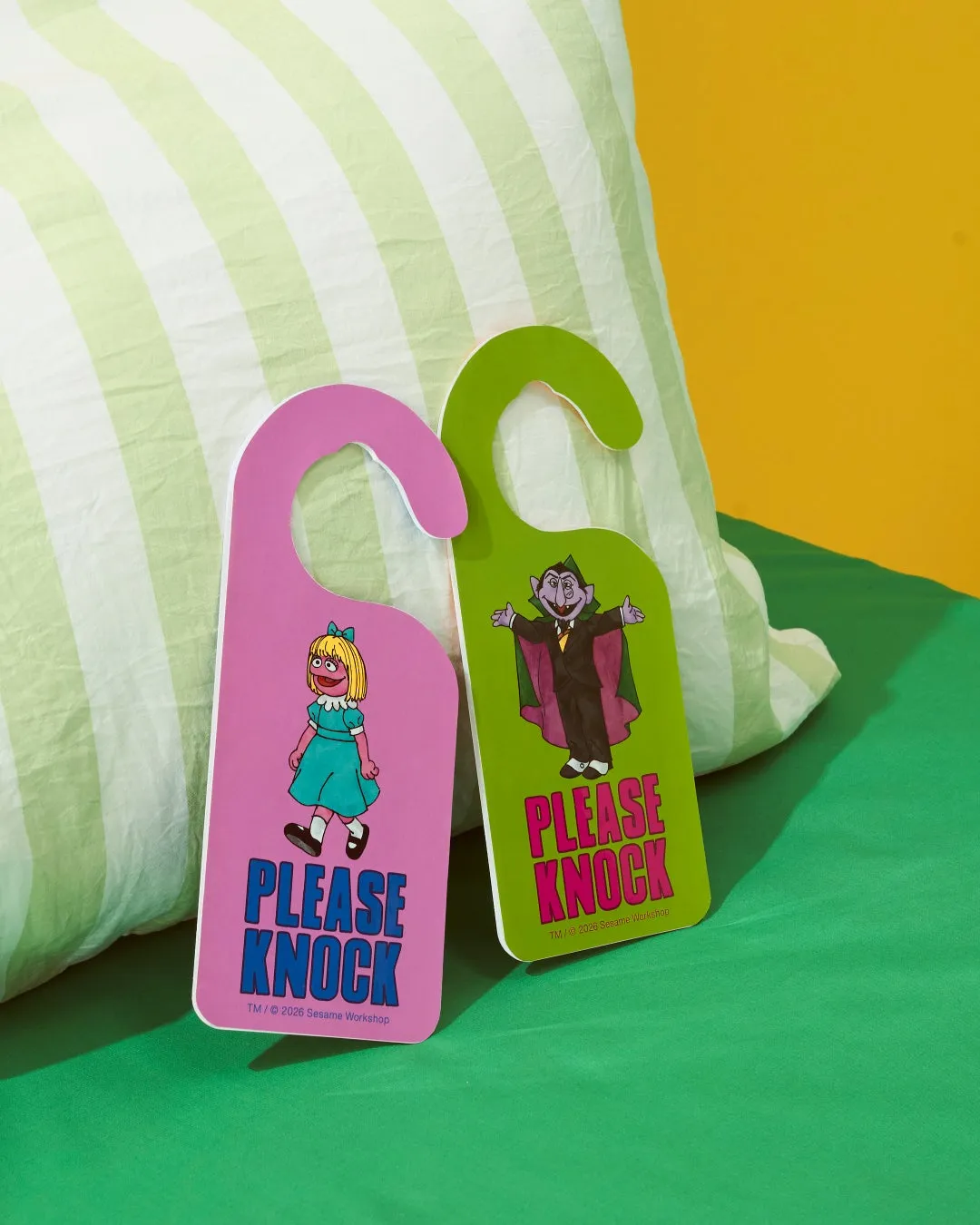 ピンクと緑のドアノブに「PLEASE KNOCK」の文字とセサミストリートのキャラクターが描かれた画像です。