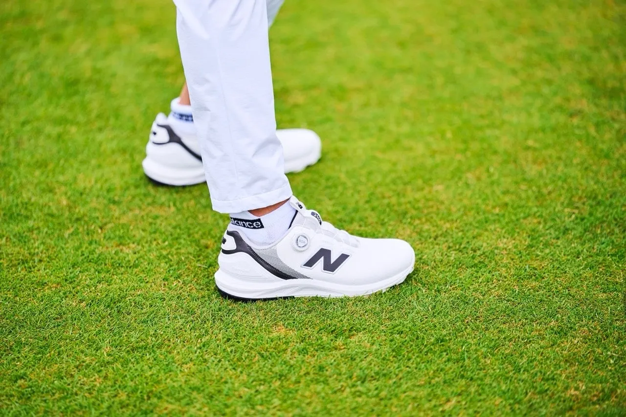 芝生の上に立つ白と黒のゴルフシューズのクローズアップ。