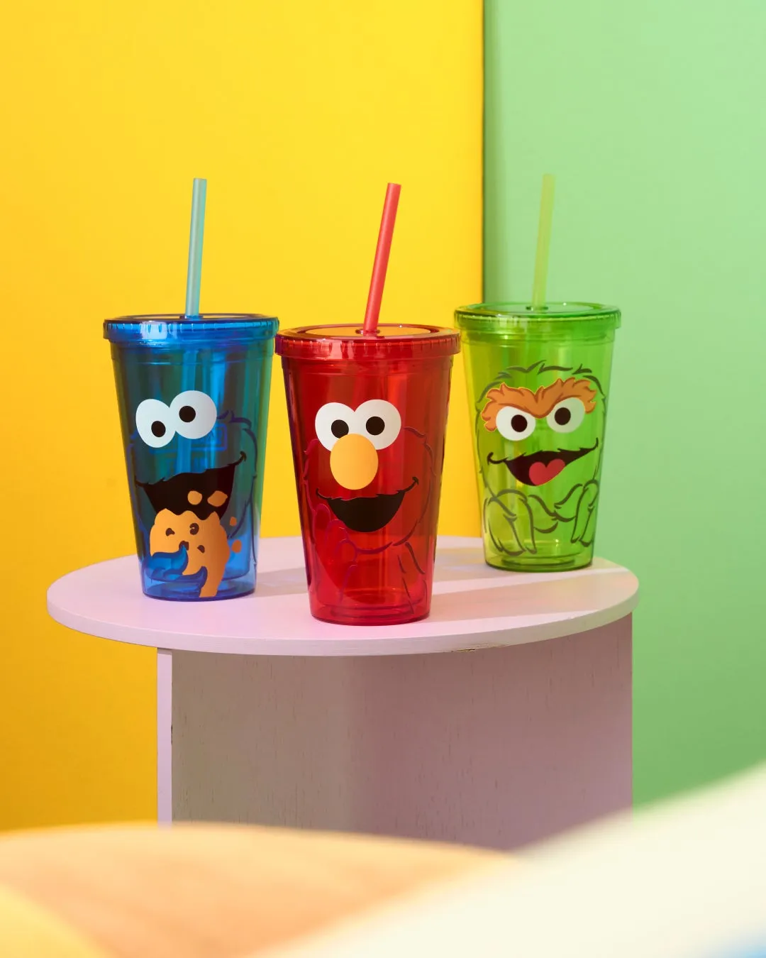 セサミストリートのキャラクターが描かれた3つのタンブラーが、丸いテーブルの上に置かれています。