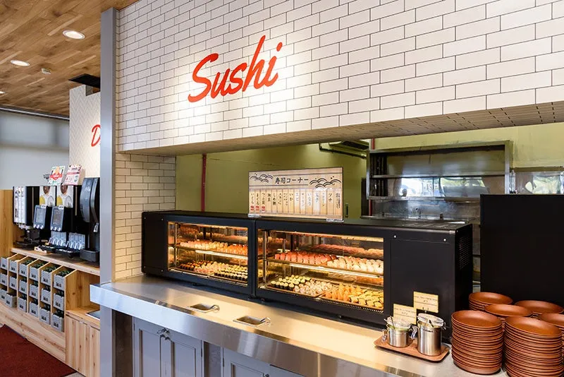 寿司を提供するレストランのカウンター。寿司が陳列されたショーケースがあり、壁には「Sushi」の文字が描かれています。